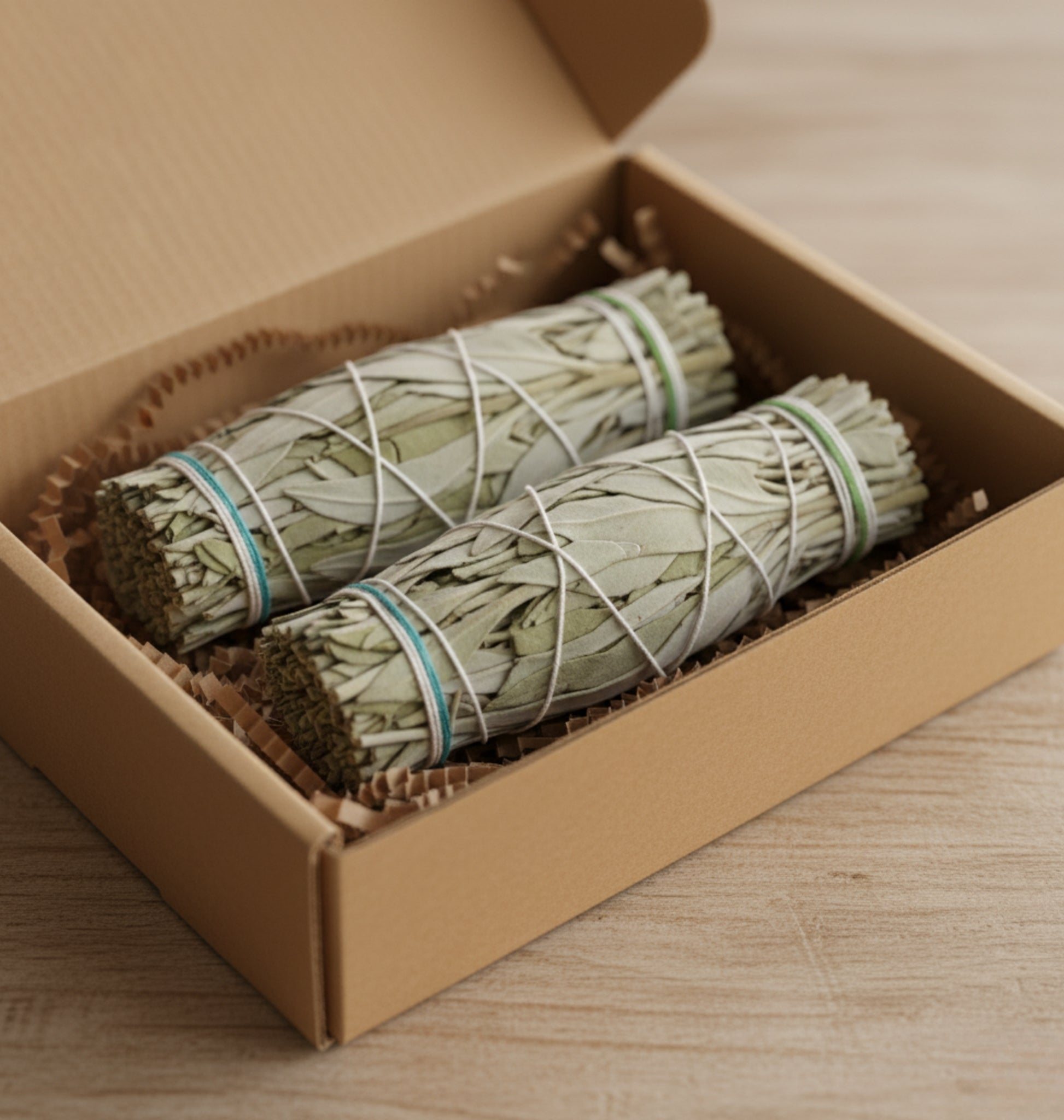 Two bundles of white sage in a cardboard gift box on a wooden surface