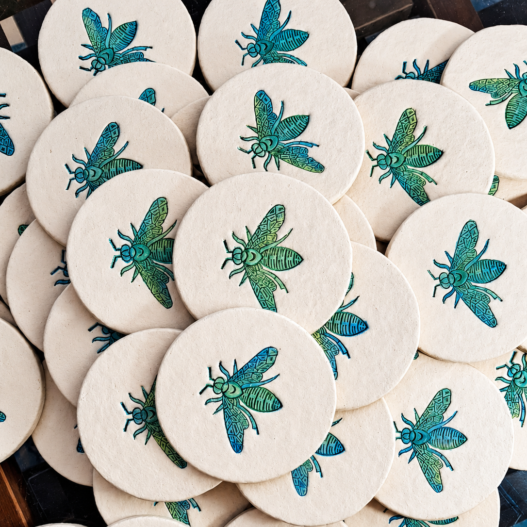 A pile of round white coasters featuring printed green and blue dragonflies, arranged closely together.