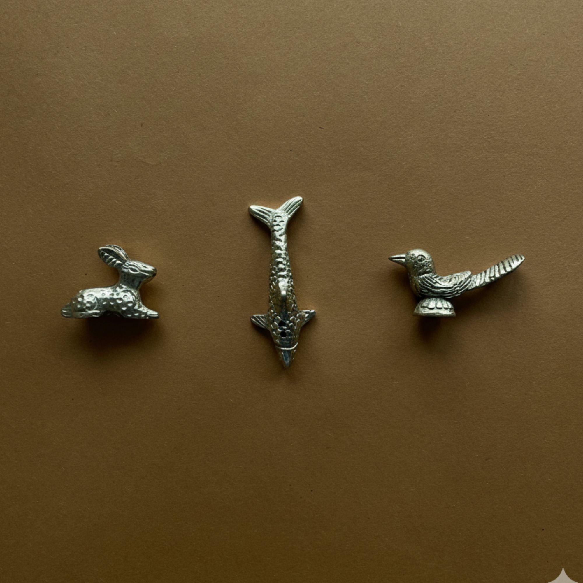 Three brass animal shaped  hare, fish and bird incense holder figurines on a brown background