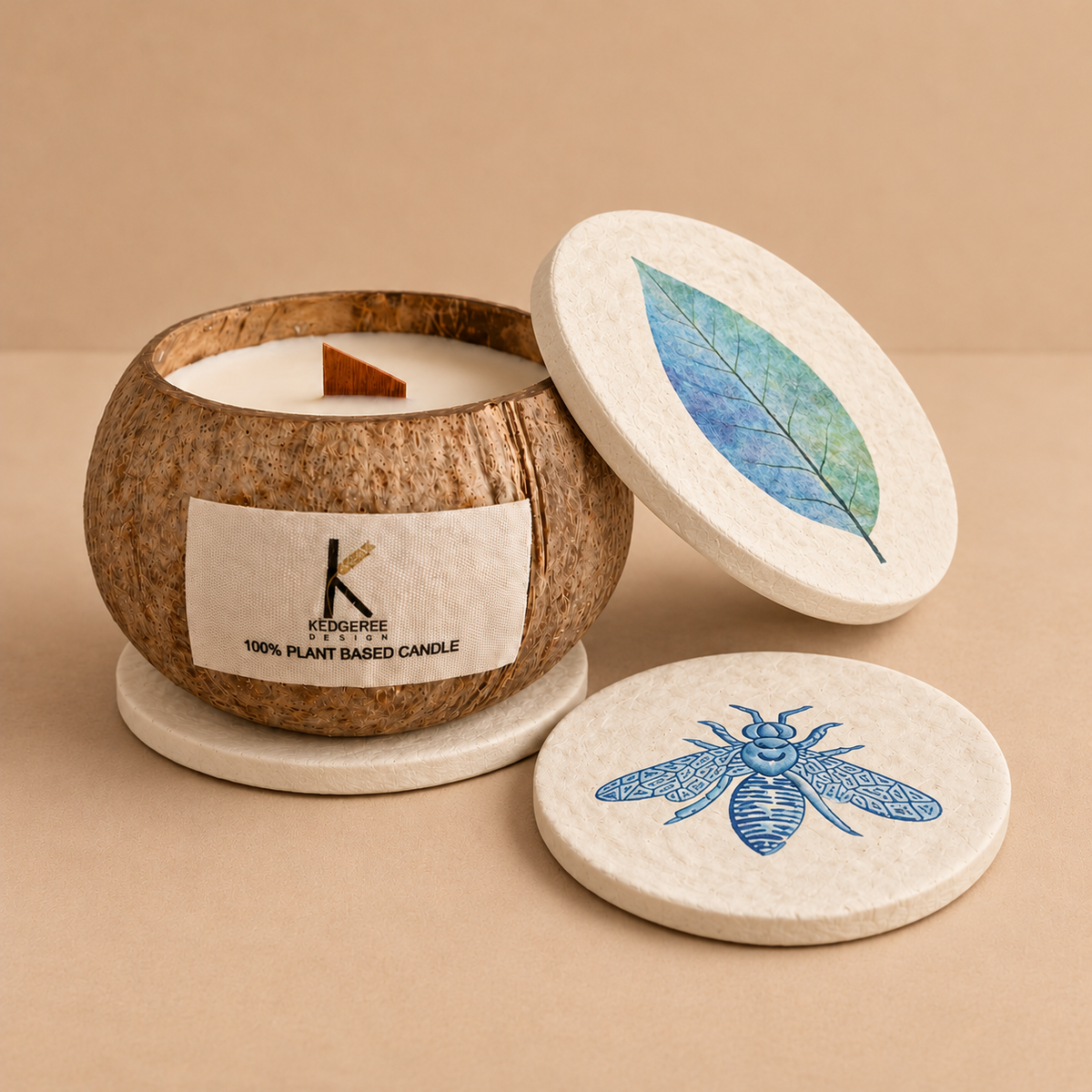 A coconut-shell candle jar with white wax and a single wick, shown open on a round coaster with its lid leaning against it. The lid and another coaster are printed with a blue leaf and a blue bee design.