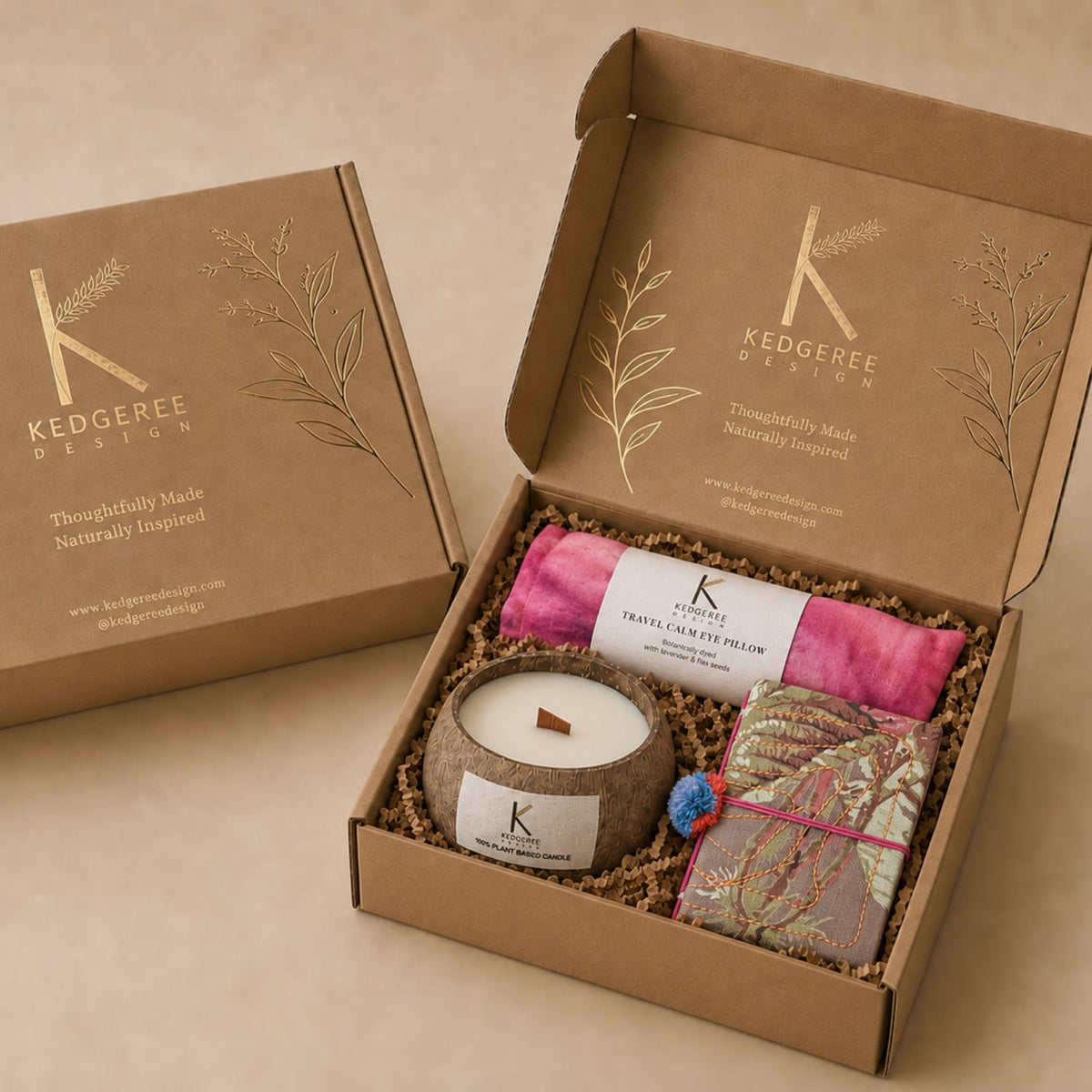 A curated gift box set from Kedgeree Design, featuring an open kraft customised box filled with a natural coconut candle, a botanically dyed eye pillow, and a handmade journal on a neutral beige background.