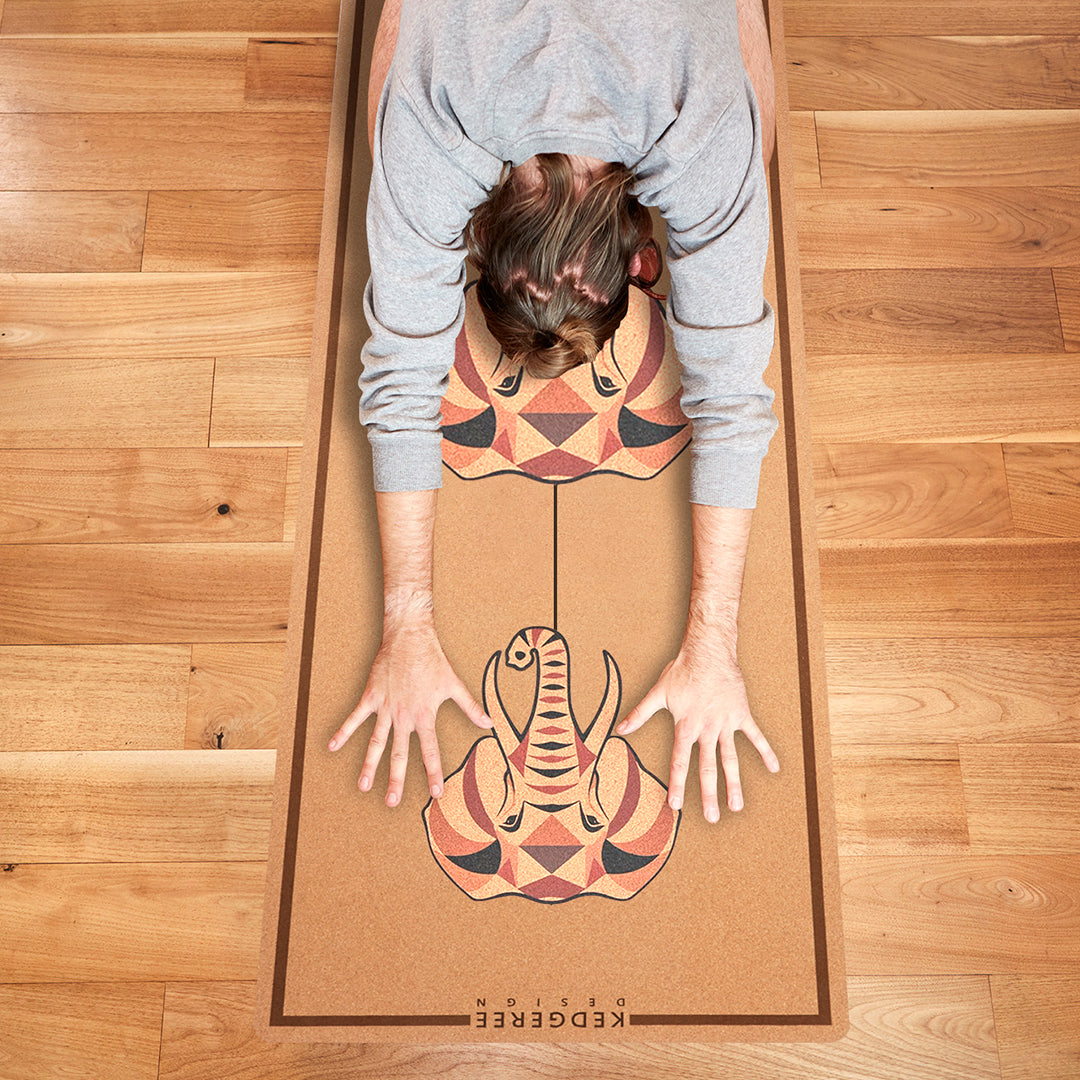 Person practicing yoga on an elephant design sustainable cork yoga mat with geometric patterns on a wooden floor.