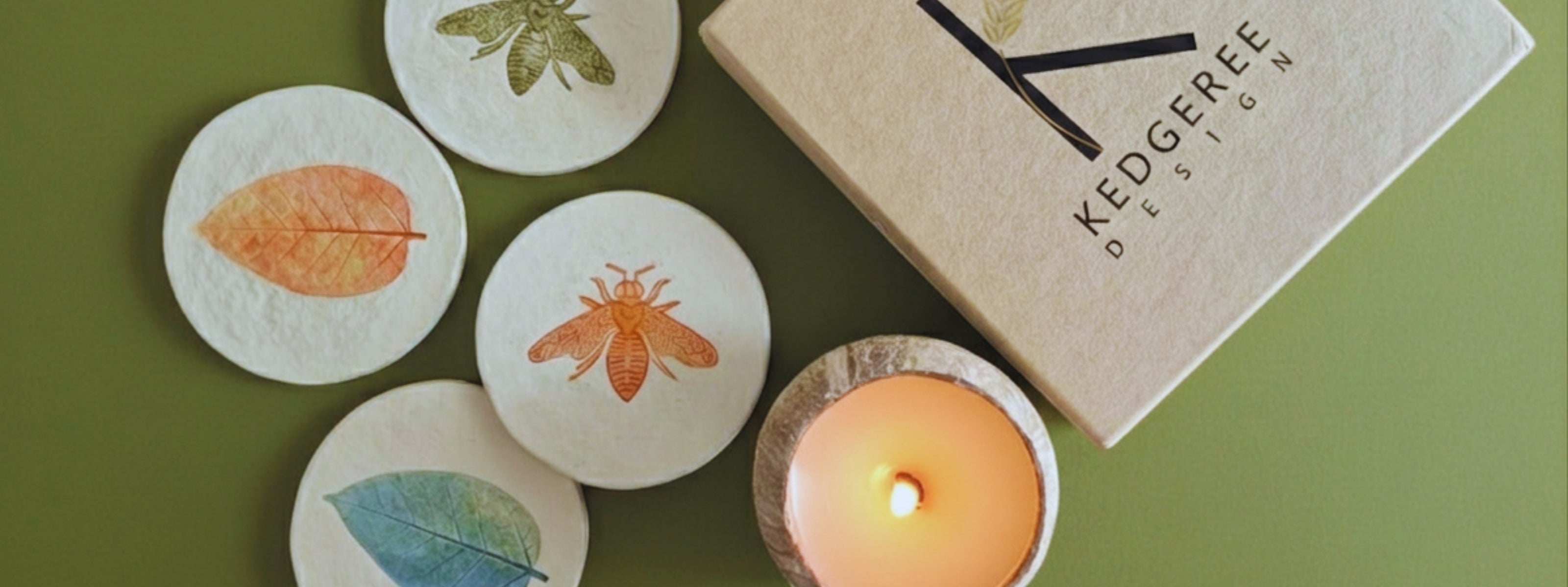 Kedgeree Design premium handmade with bee and leaf-patterned coasters and a lit candle on a green background