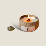 Kerala Serenity coconut shell candle with a burning wick, hand-poured in a natural coconut shell with plant wax and essential oils. The candle has a fresh and calming scent, a unique and stylish design, and comes with a wooden lid.