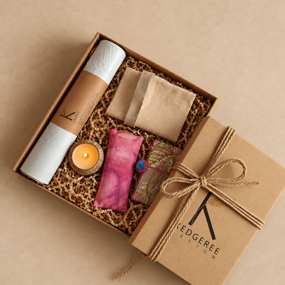 A curated Yogi Gift set by Kedgeree Design includes a yoga mat, candle,  eye pillow, journal, yoga bag and a gift box on a brown background.