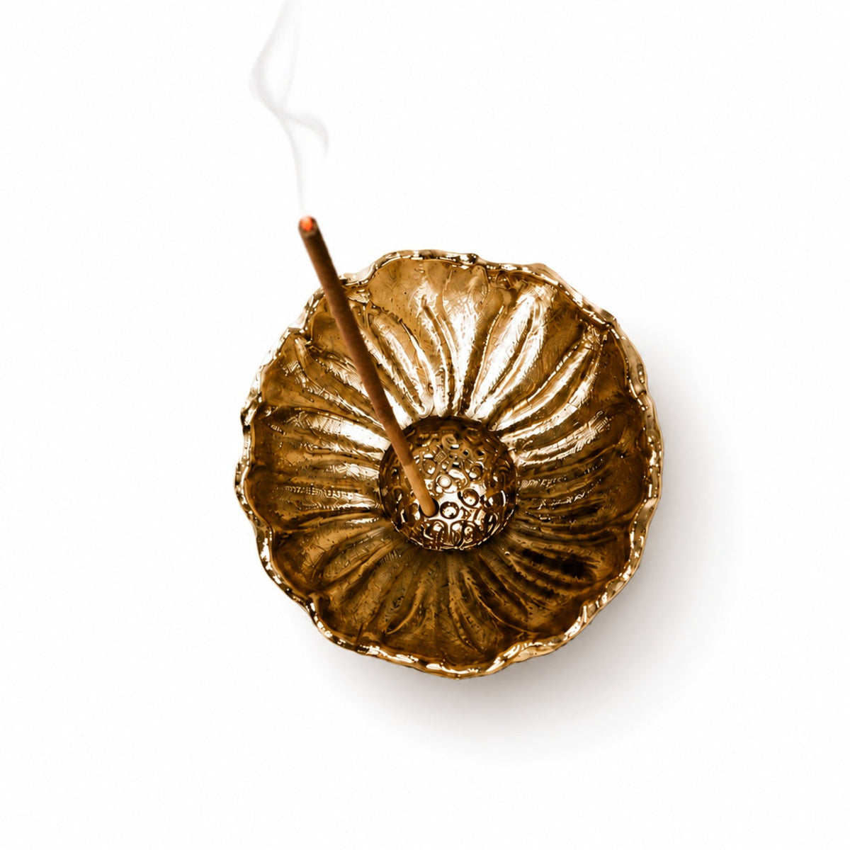 A brass gold lotus-shaped incense holder with a single incense stick resting inside, set against a plain white background with a soft shadow and wisps of smoke.